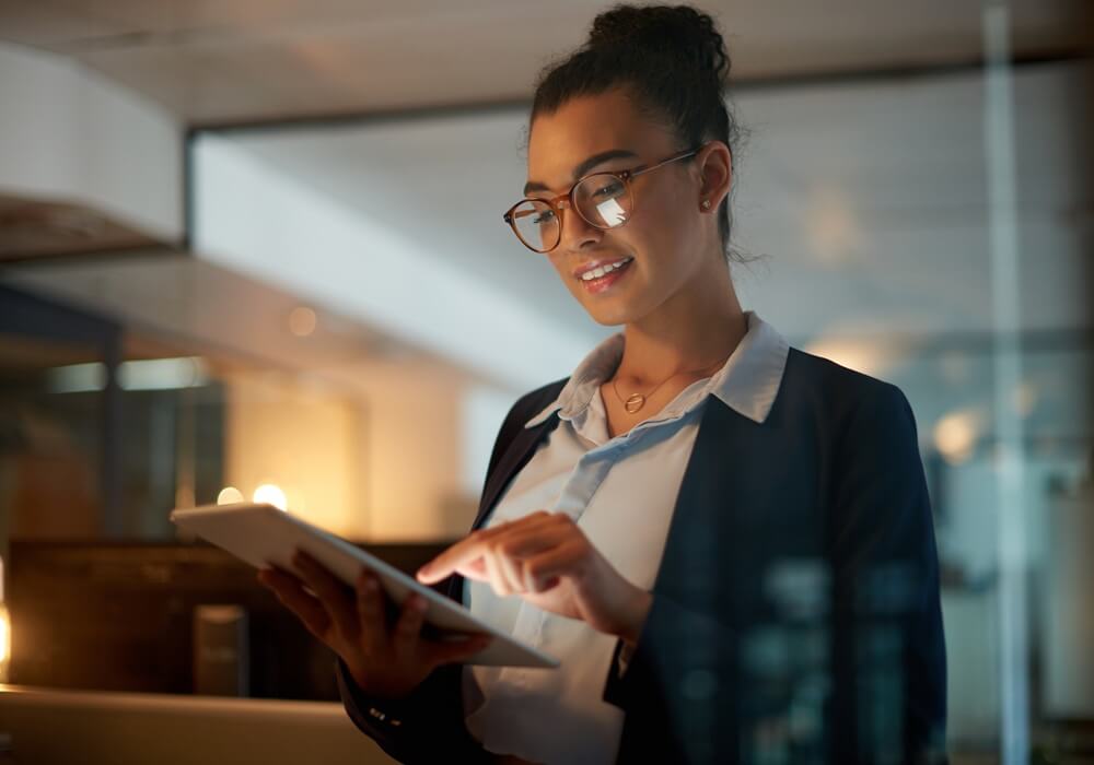 Woman in business attire using a tablet in a warmly lit modern interior.